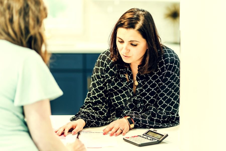 Empregada doméstica conversando com cliente e anotando valores em uma agenda.